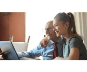 Older gentleman sitting with younger woman looking at a computer screen together
