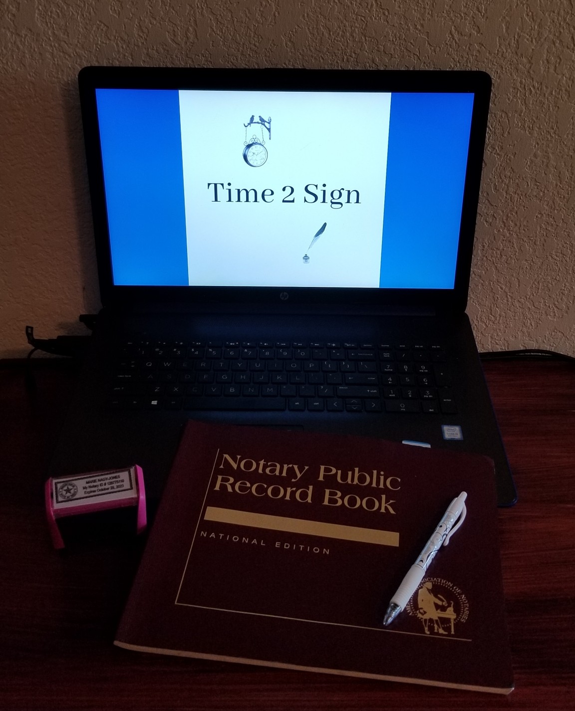 Laptop on and open with old logo on screen, Notary Journal, Pen lying on journal, Notary Stamp